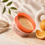 Pastel creamy scrub with Orange and Vitamin C placed beside fresh oranges and soft floral decor in a luxury skincare setup