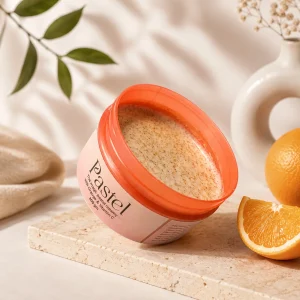 Pastel creamy scrub with Orange and Vitamin C placed beside fresh oranges and soft floral decor in a luxury skincare setup